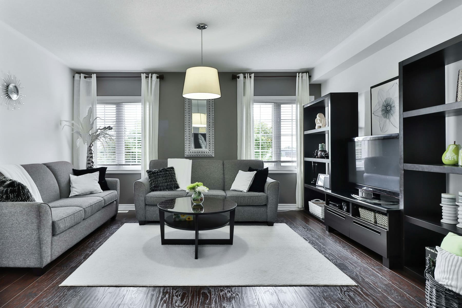 Wohnraum mit Sofa, hellen Vorhängen und dunklem Riemenboden